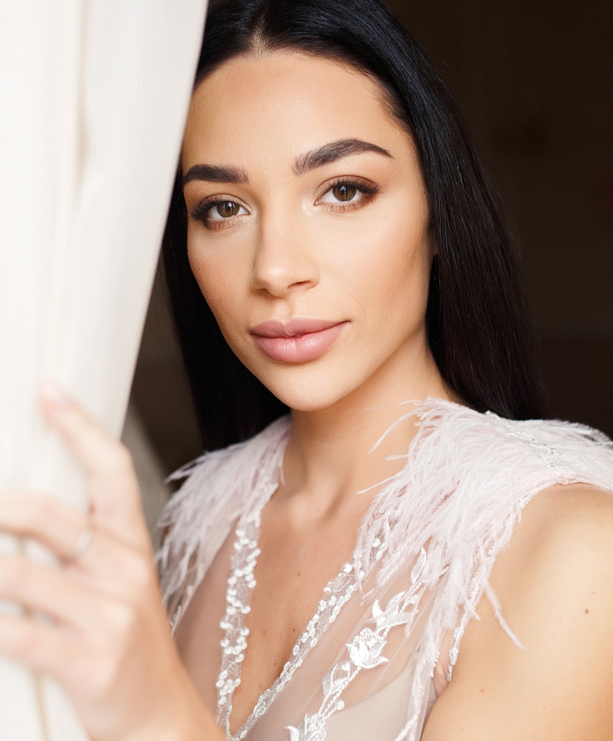 Woman with long black hair near a curtain.