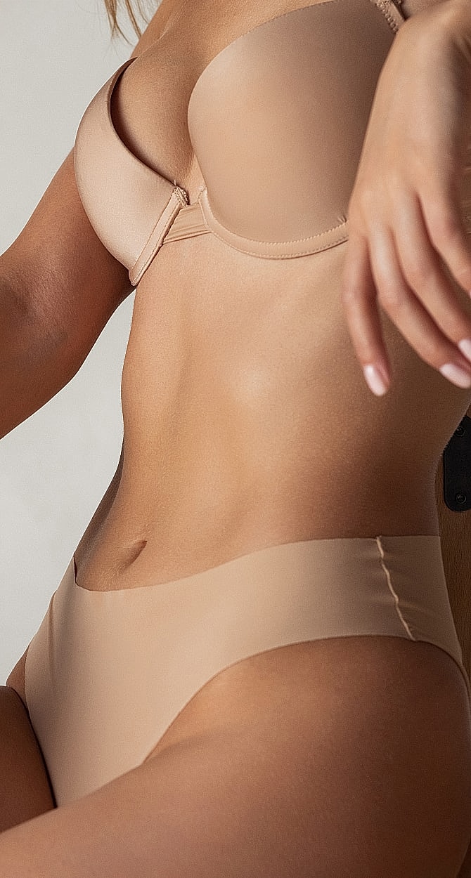 Model wearing nude lingerie in studio setting.