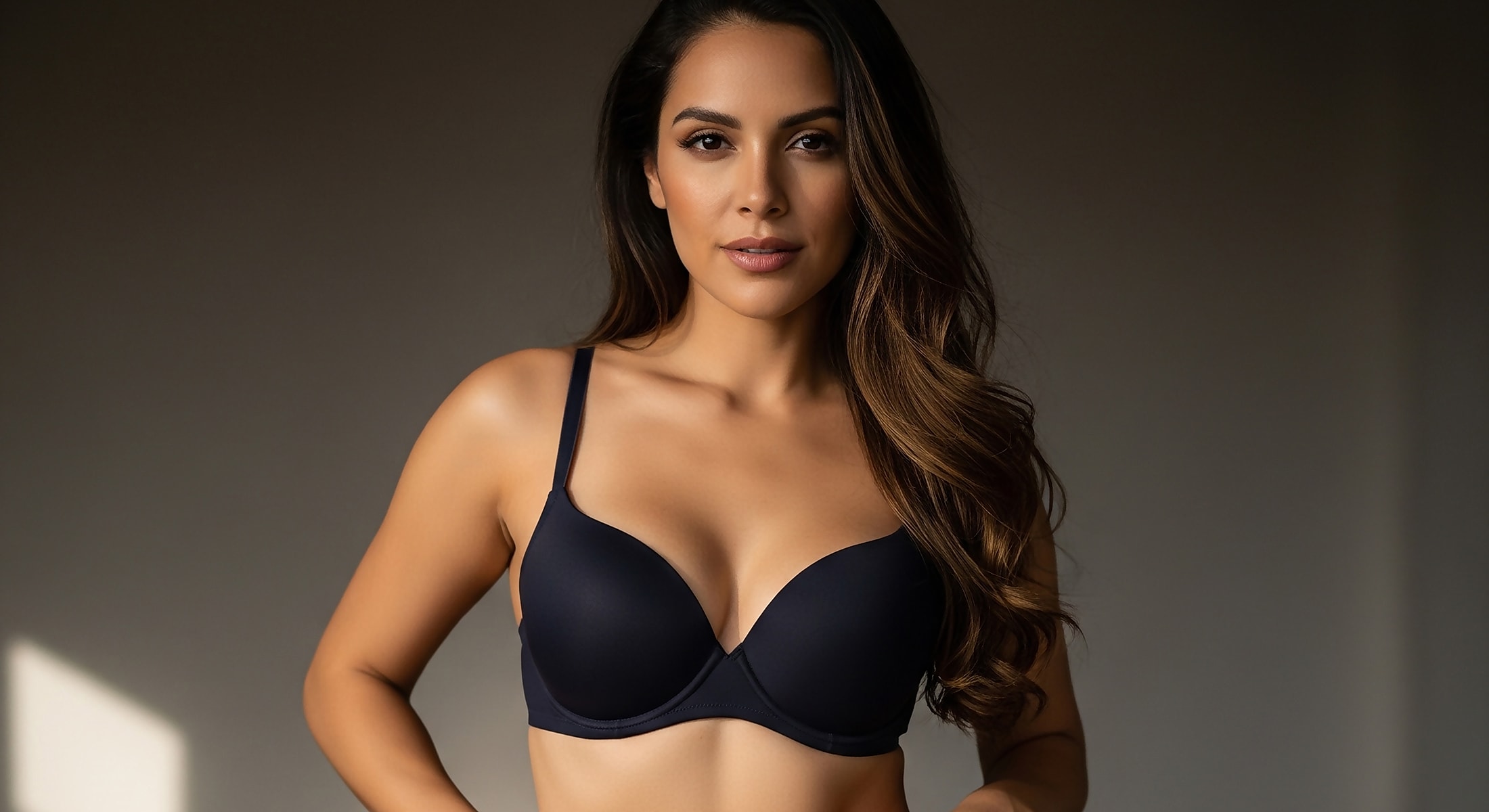 Model posing in dark bra against neutral background.