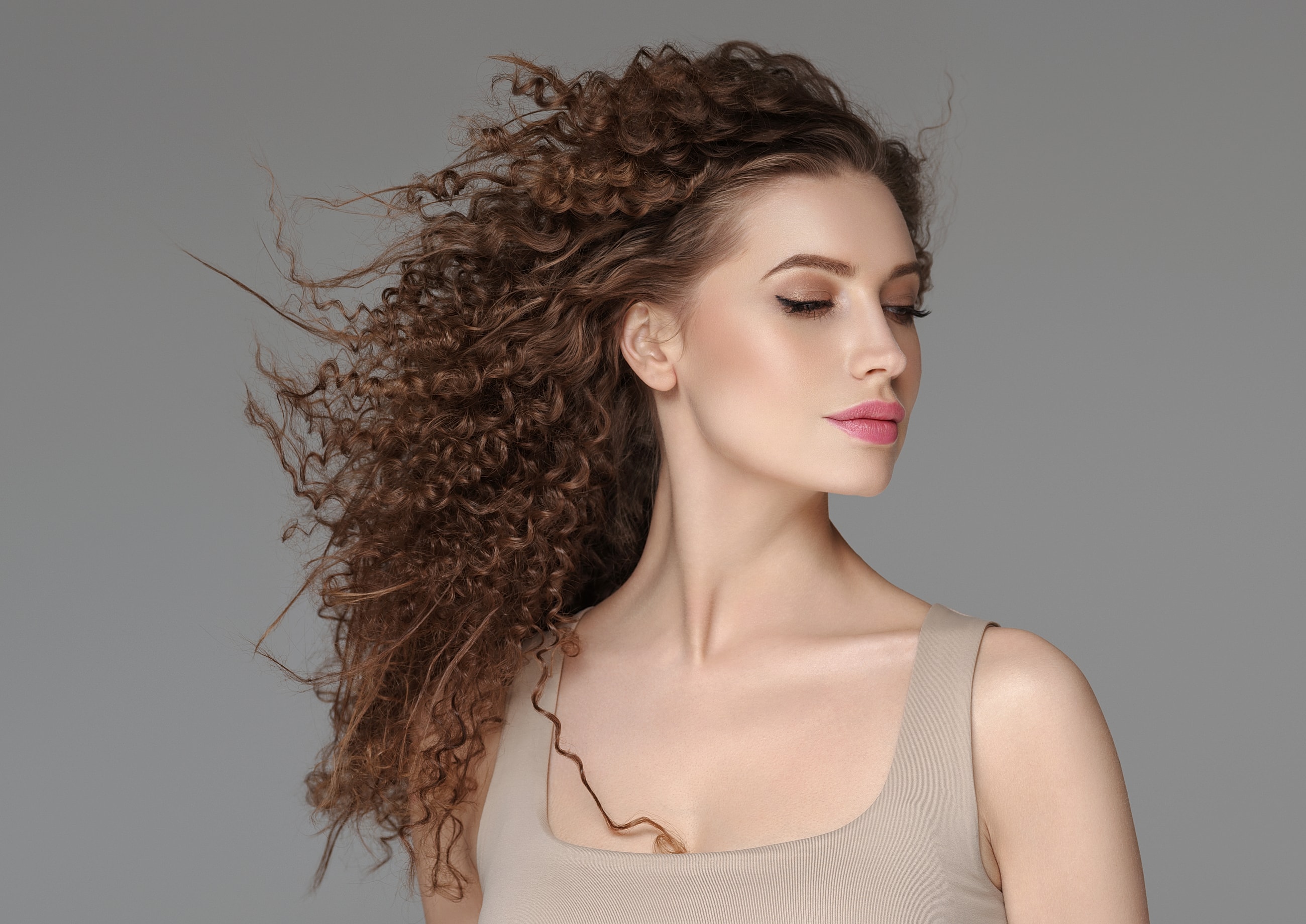 Model with curly hair against gray background.